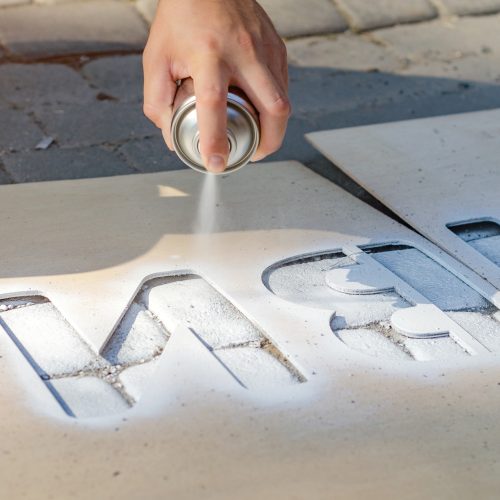 Hand holds an aerosol spray can, puts the image on the asphalt through a stencil